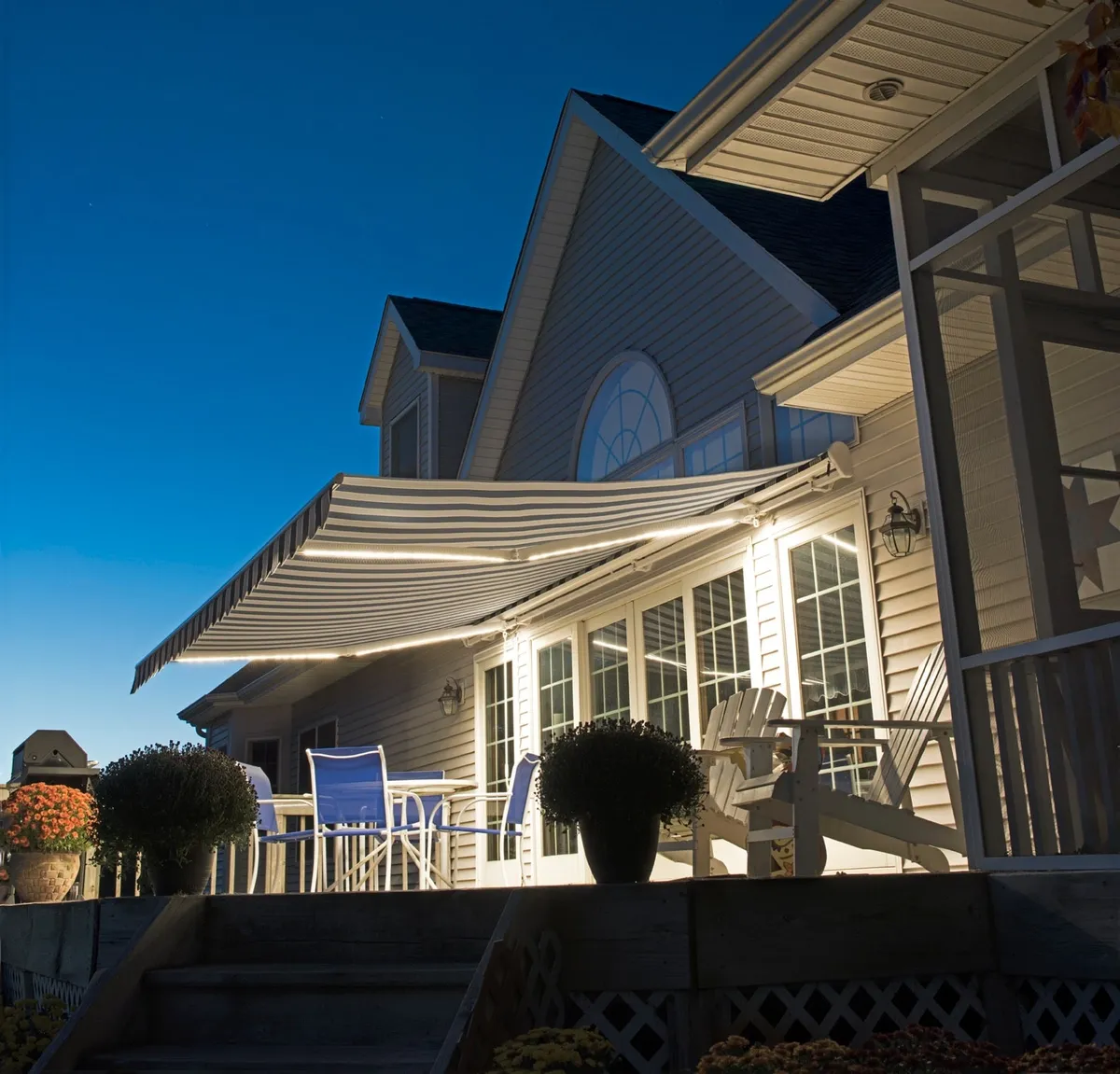 SunPro retractable awning with built-in LED arm lights glowing over a deck at dusk.